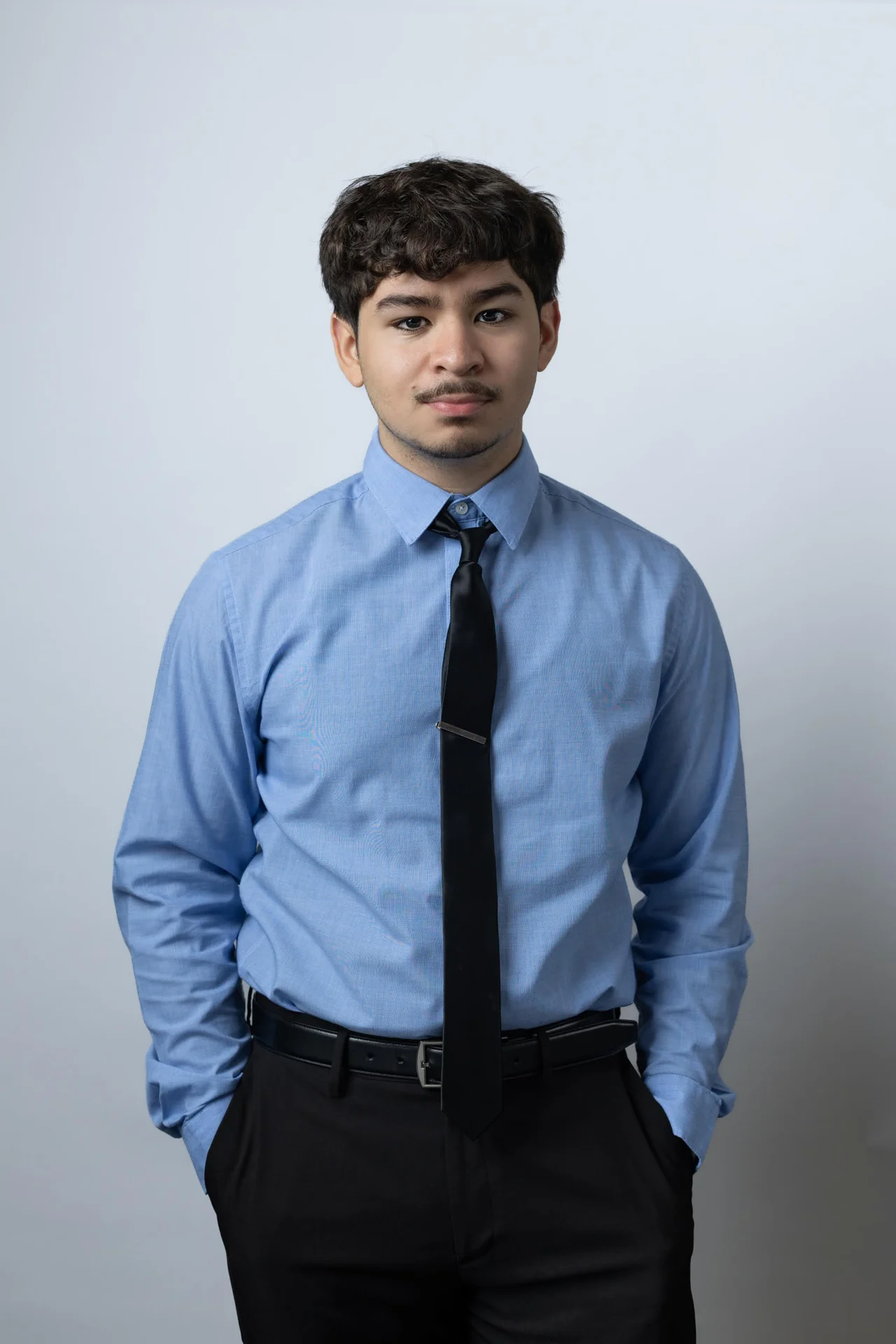 Retrato de un joven con camisa celeste y corbata negra en estudio